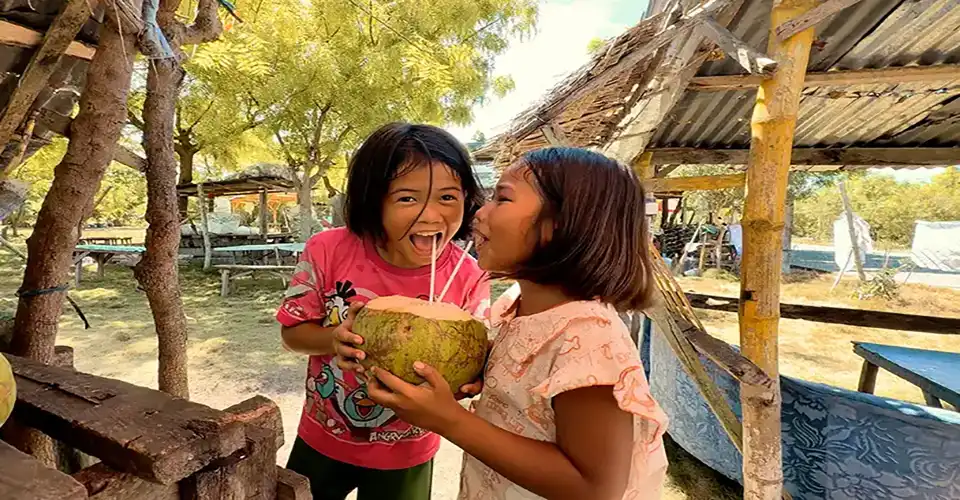 Two kids sharing a fresh coconut drink at a market on Olango Island